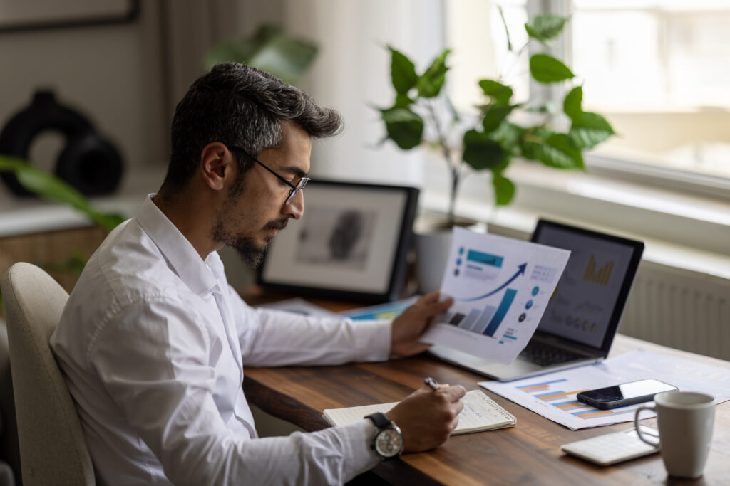 A man with glasses writing and reviewing growth charts at his desk.