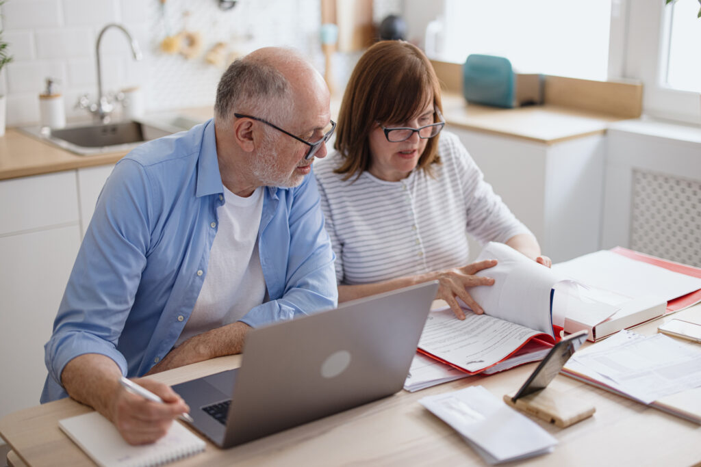 Retired couple reviewing paperwork and a laptop at their kitchen table