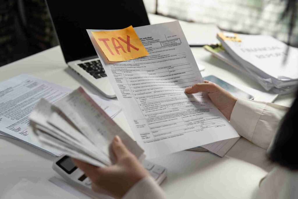 A person holding tax documents with a sticky note labeled "TAX."